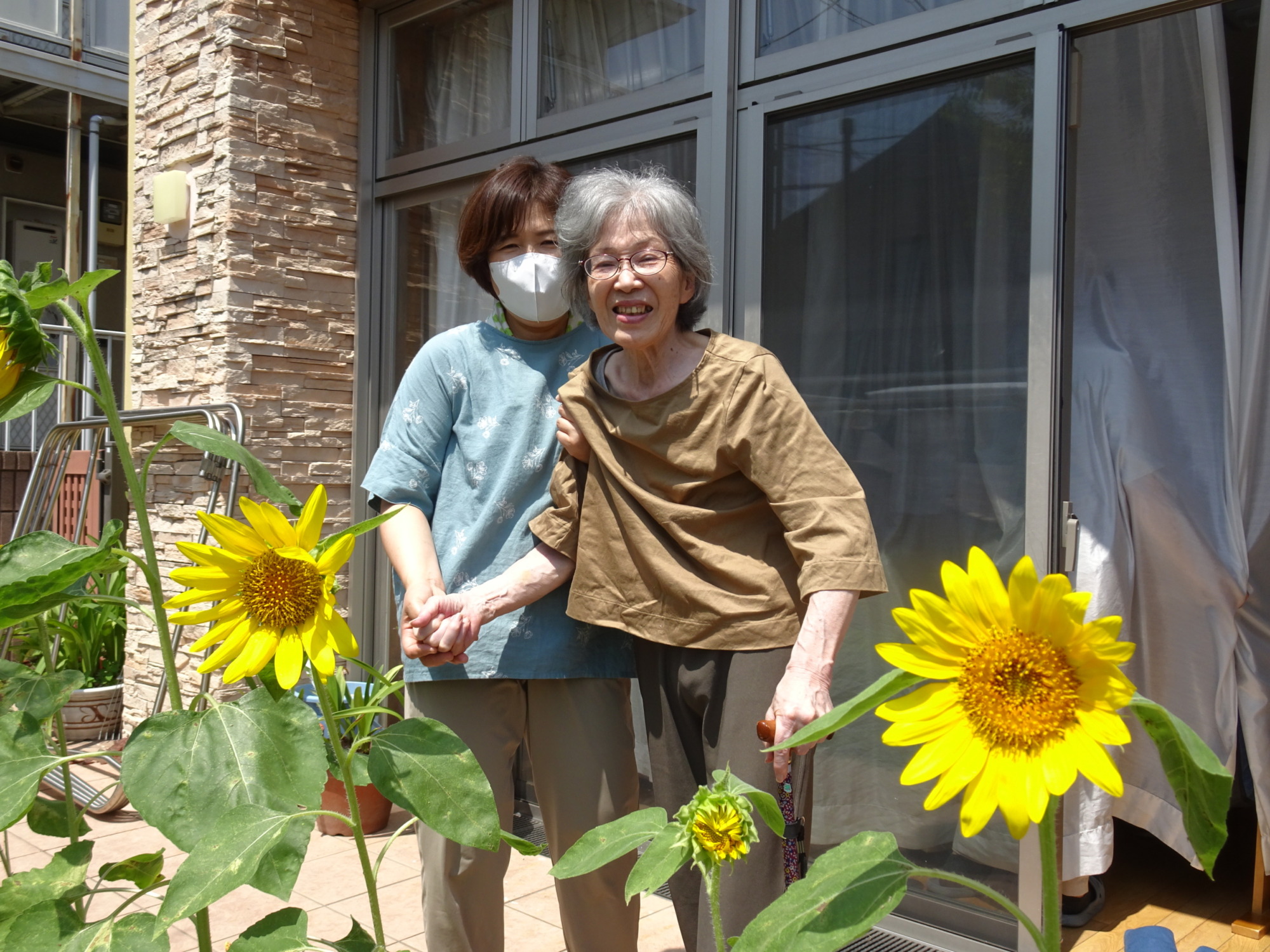 ひまわりと一緒に写真を撮る利用者さんとワーカー