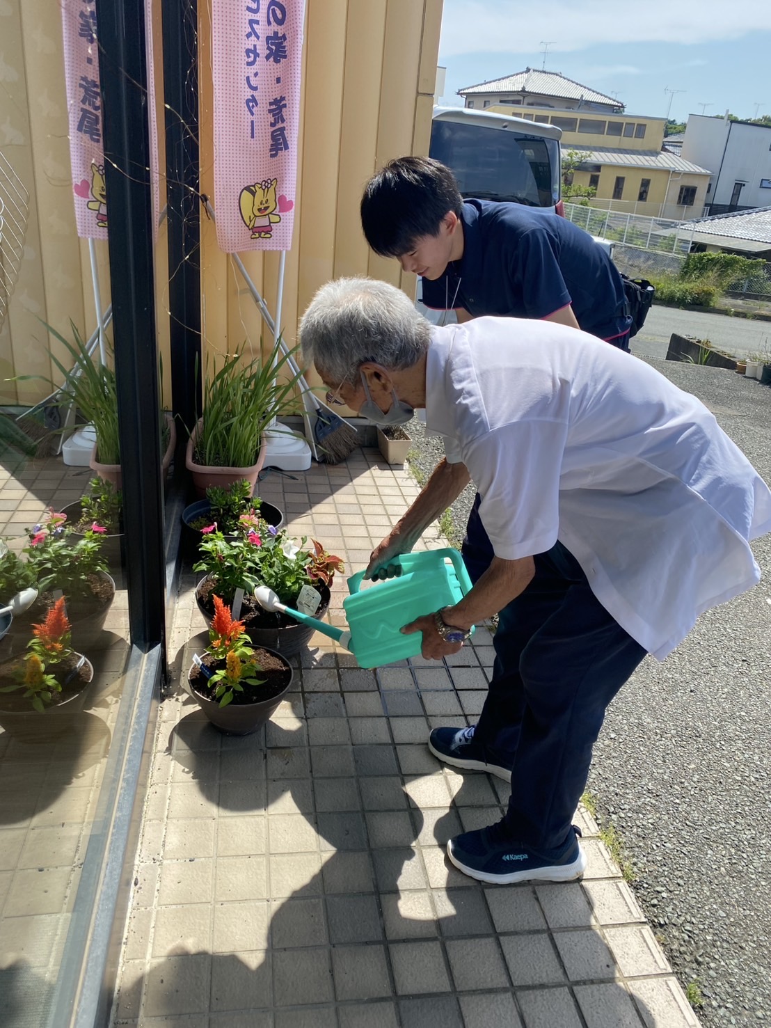 学生と一緒に鉢に水をかけている高齢者