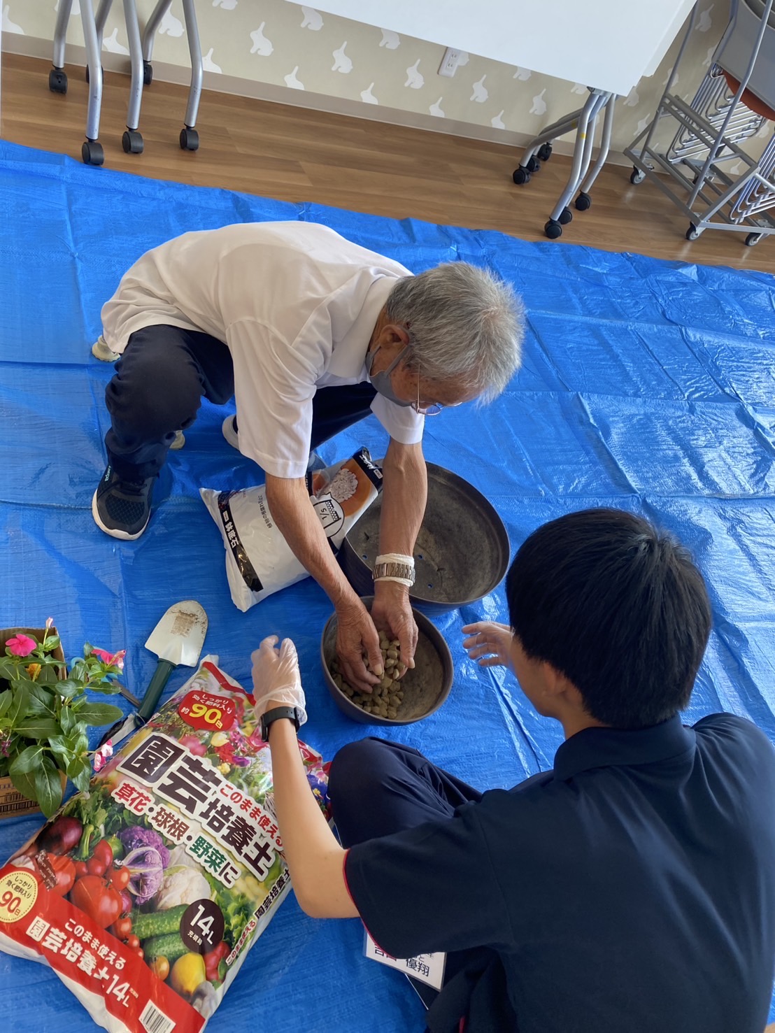 鉢に石をいれている高齢者それを見守る学生