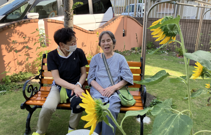 庭のベンチに座ってひまわりを眺める利用者さん