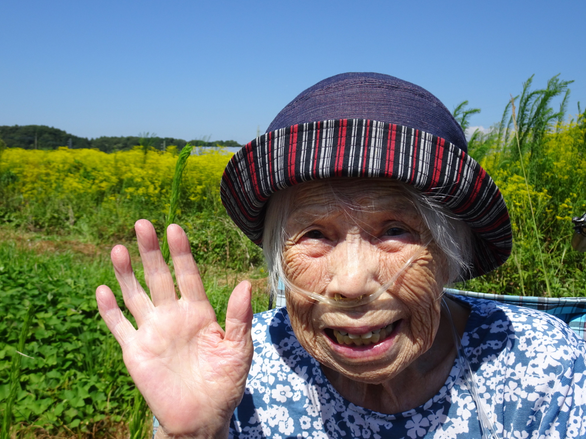 黄色の花が咲く畑の前で笑顔で写る利用者さんの写真
