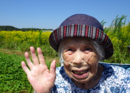 黄色の花が咲く畑の前で笑顔で写る利用者さんの写真