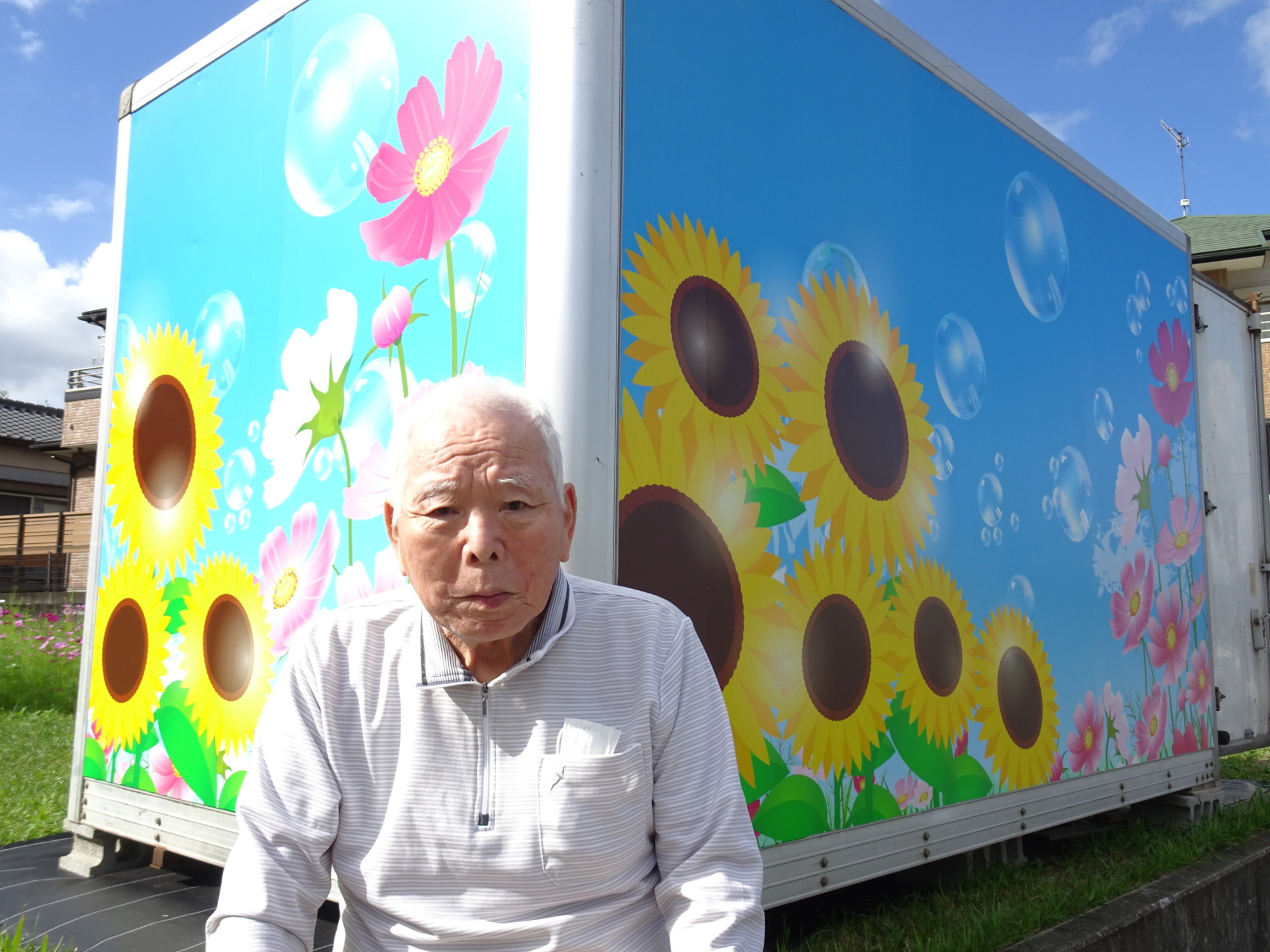 ひまわりの絵が描かれたコンテナの前で撮った利用者さんの写真