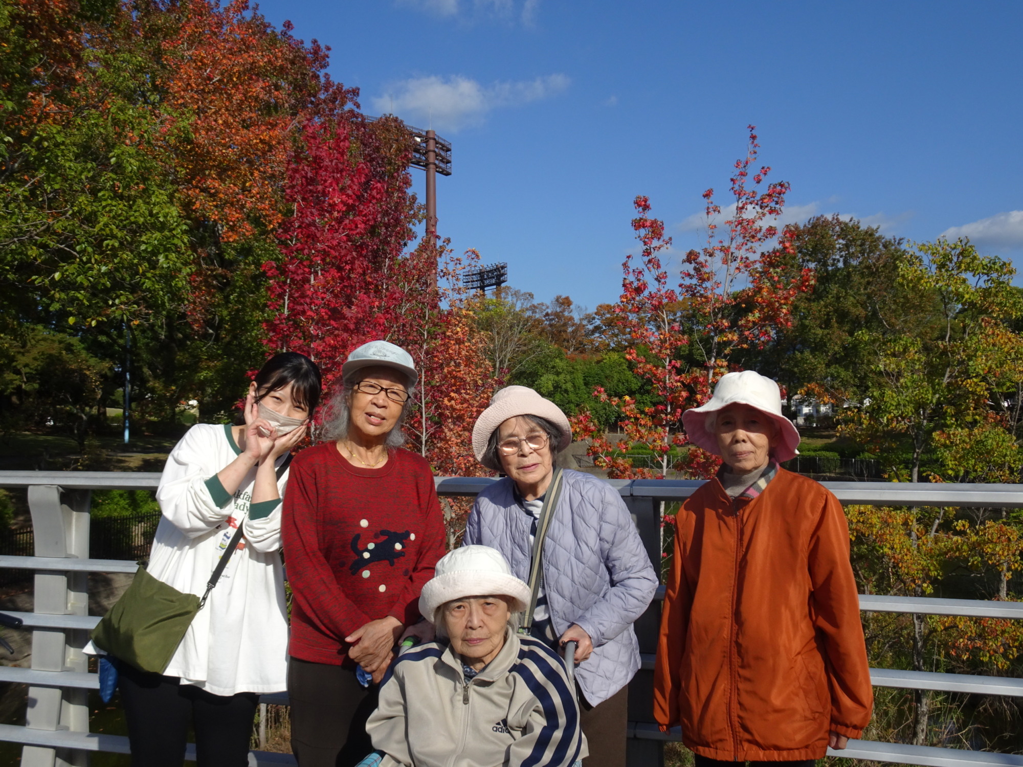 春日公園内の橋の上で紅葉をバックに撮った利用者さんたちとワーカーの写真
