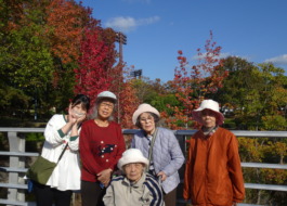 春日公園内の橋の上で紅葉をバックに撮った利用者さんたちとワーカーの写真