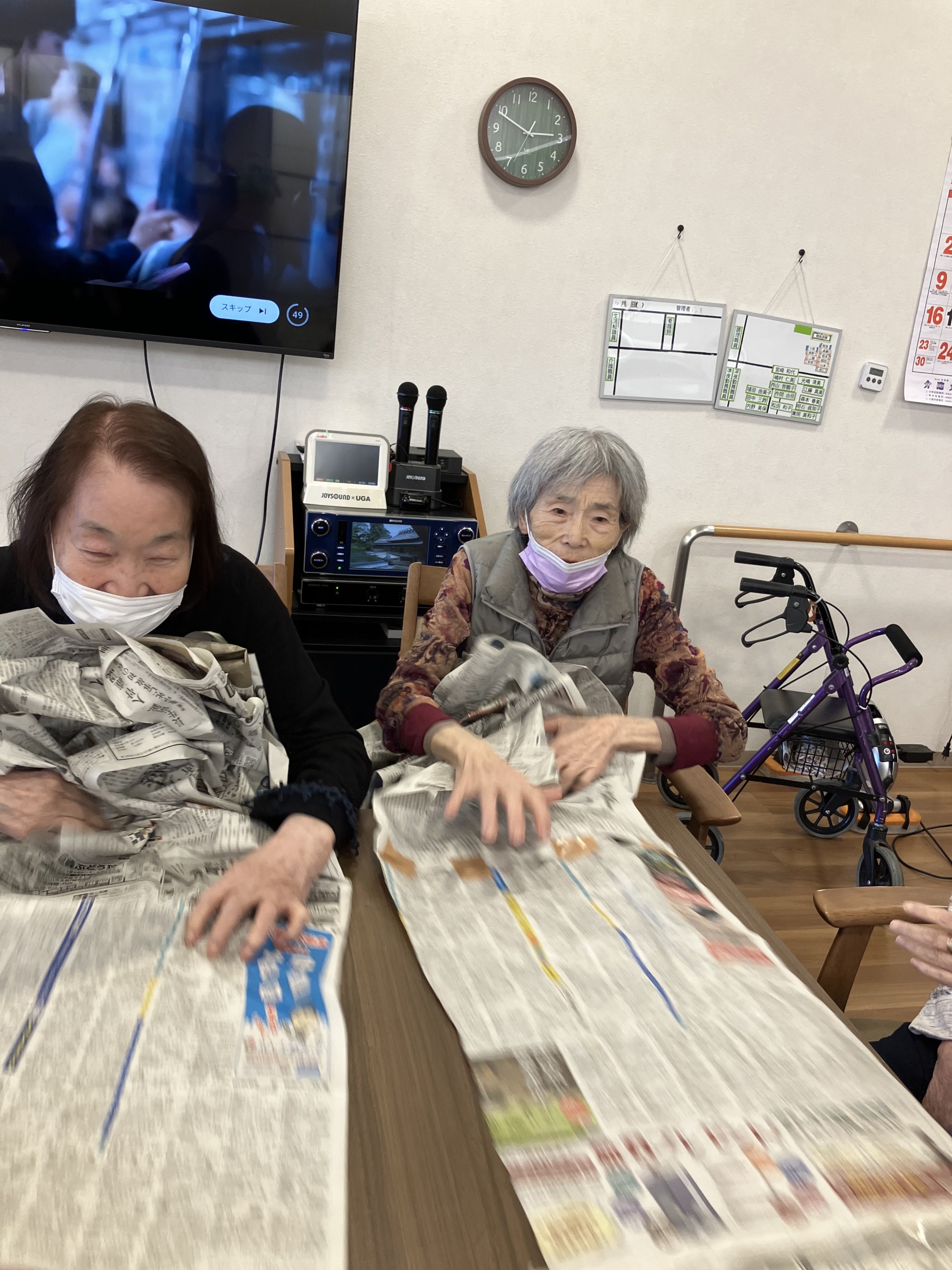 長くつないだ新聞紙を手で手繰り寄せている高齢者二人