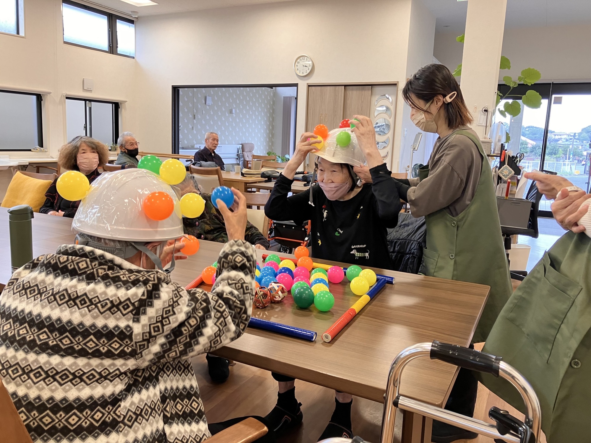 カラーボールをヘルメットにつけて競争する高齢者二人。それを見守るスタッフ