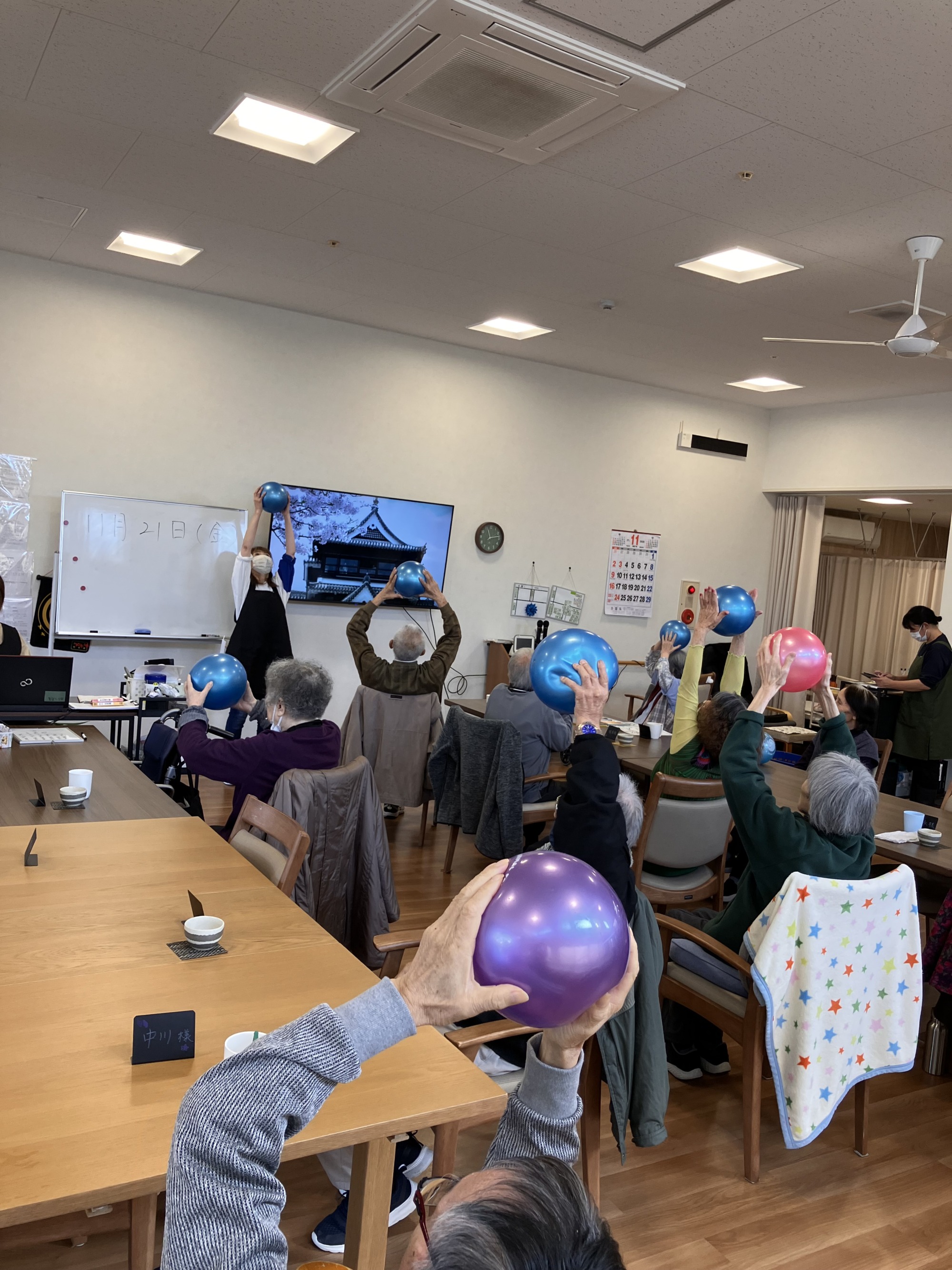ホールで高齢者数名とスタッフでボール体操をしている様子
