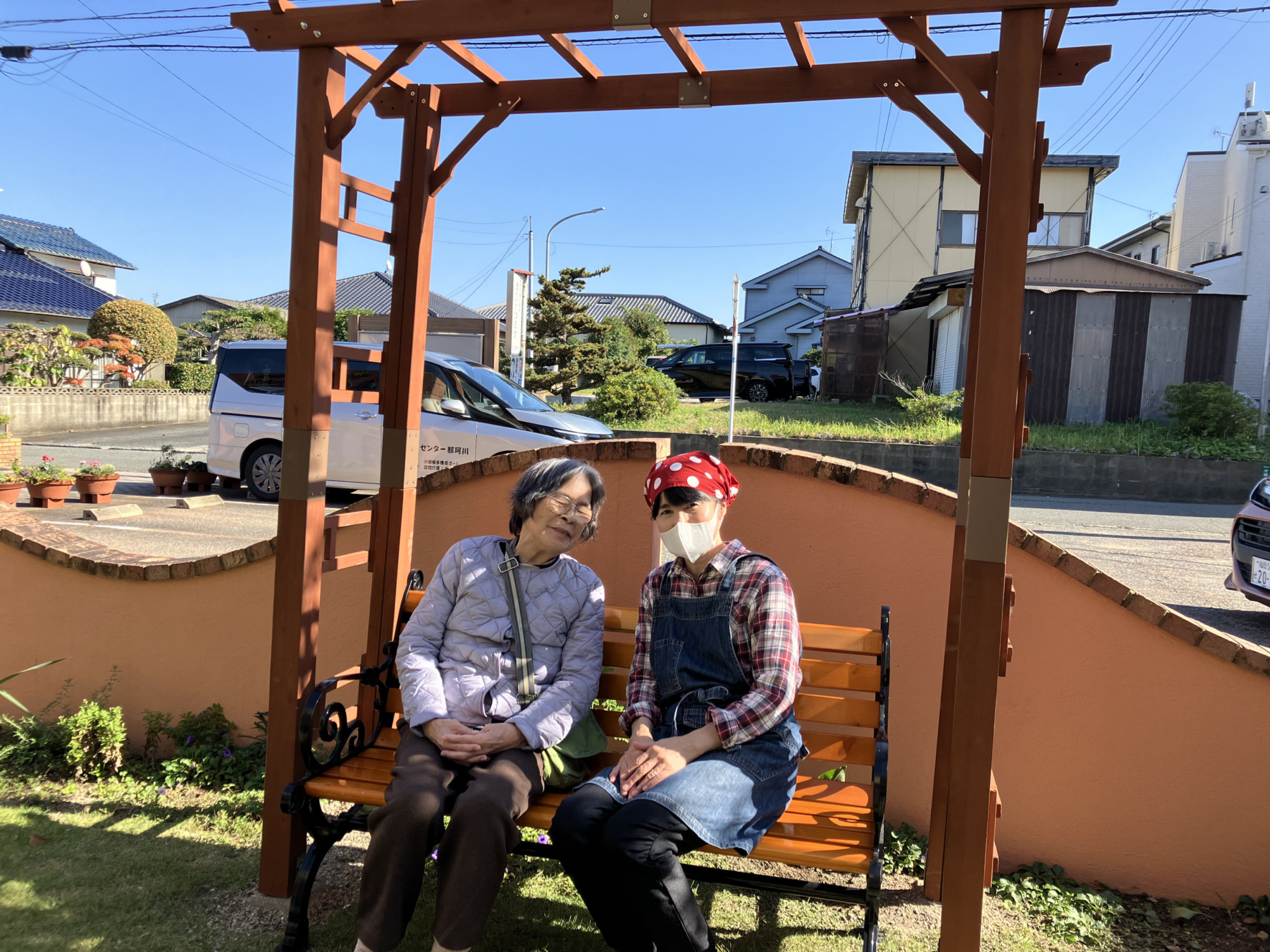 パーゴラの下のべんちでワーカーと日向ぼっこする利用者さん