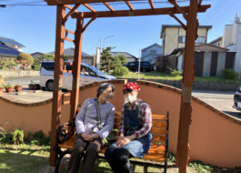 パーゴラの下のべんちでワーカーと日向ぼっこする利用者さん