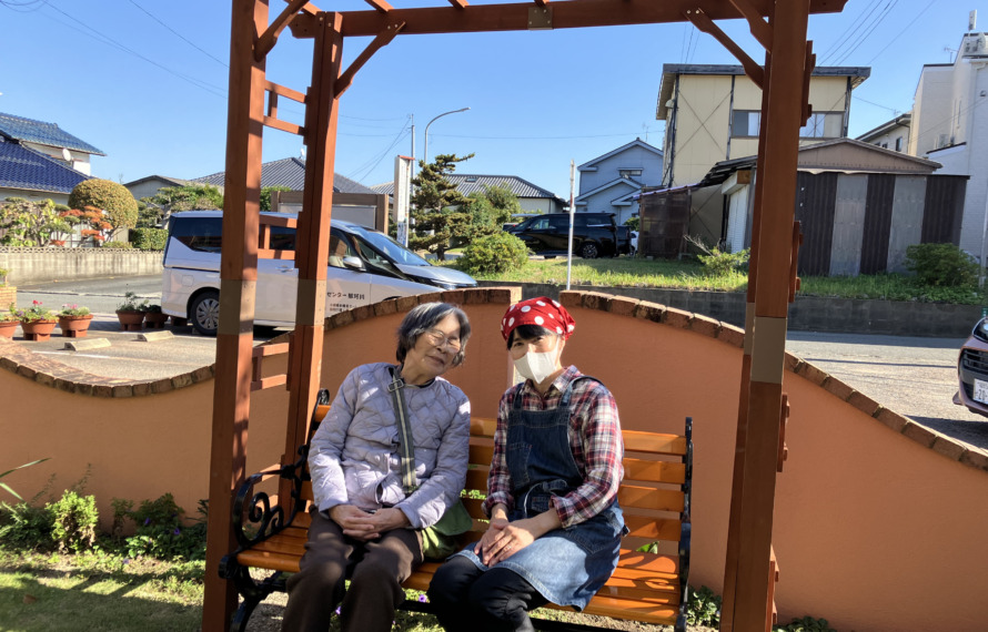 パーゴラの下のべんちでワーカーと日向ぼっこする利用者さん