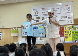 食材がどのようにして食事としてテーブルまで届くかということを保育士と給食職員が子ども達に説明をしています。