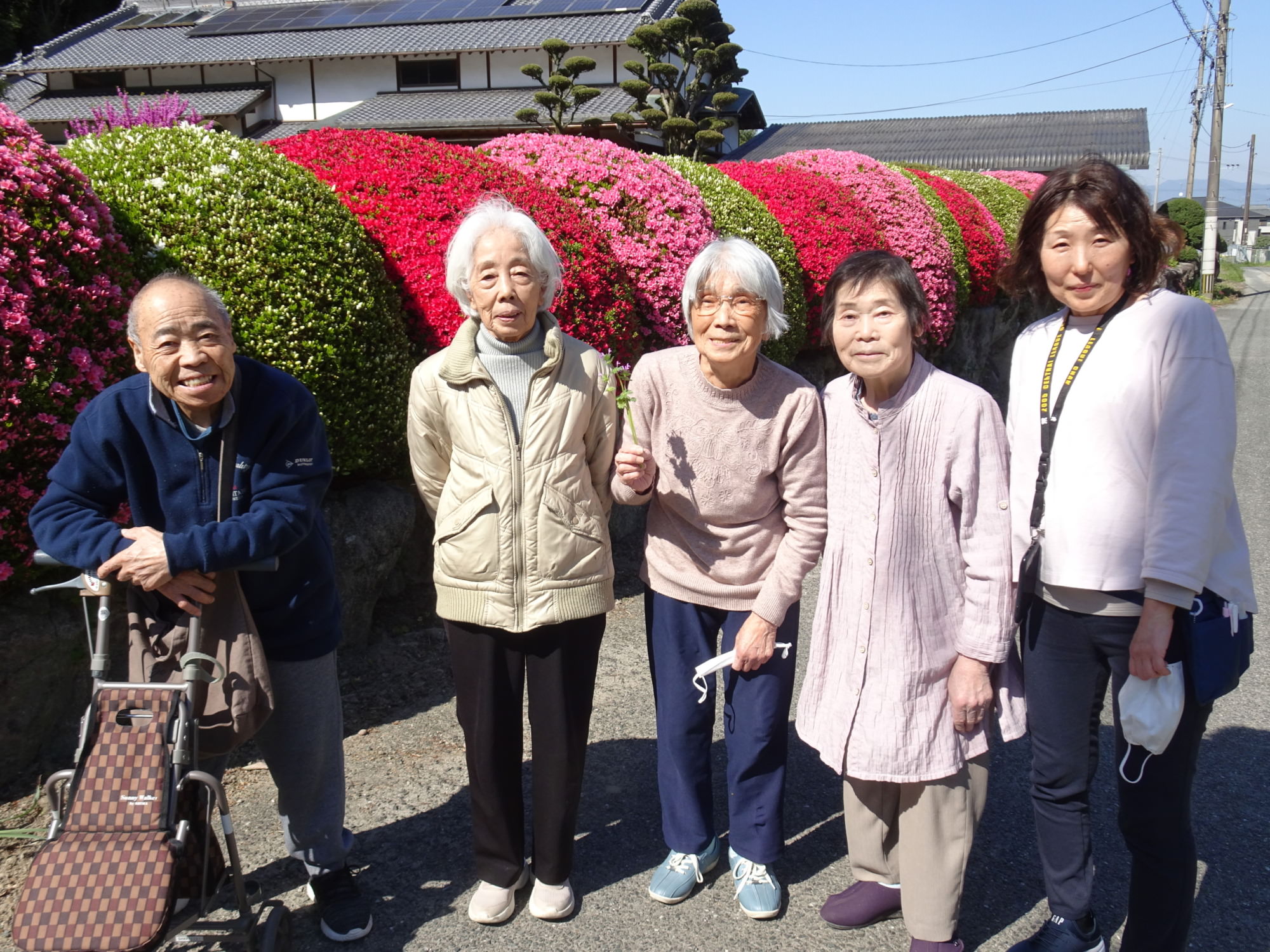 赤とピンクのツツジの前で撮った利用者さんたちの写真