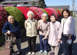 赤とピンクのツツジの前で撮った利用者さんたちの写真