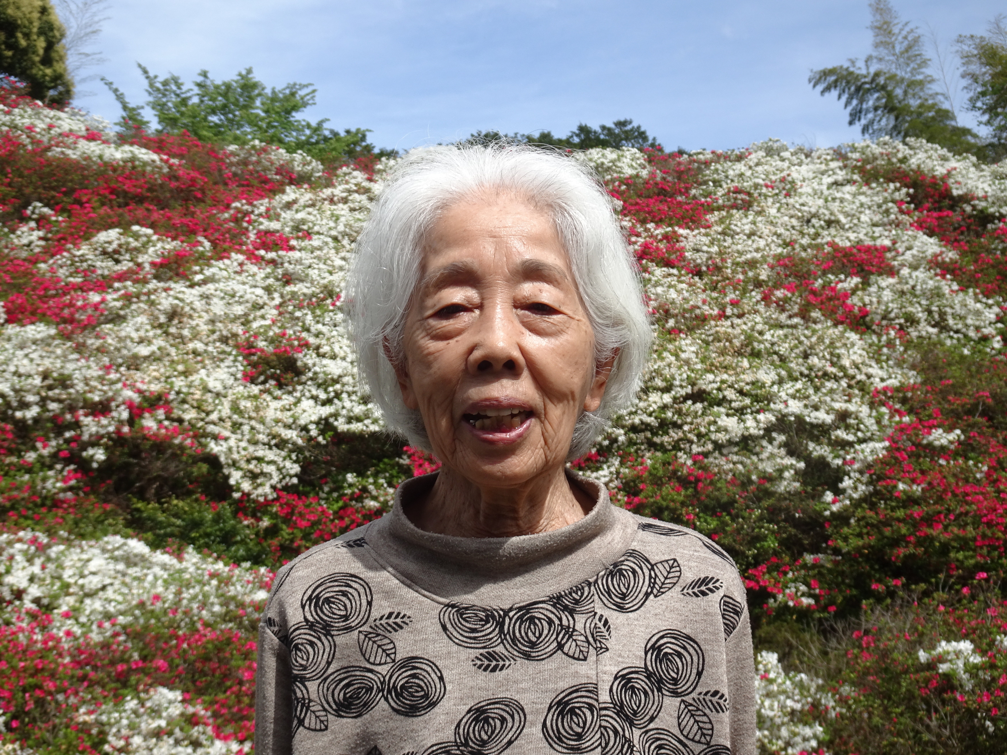 赤や白のツツジをバックに撮った利用者さんの写真