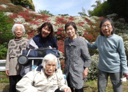 赤や白のツツジをバックに撮った利用者さんたちとワーカーの写真