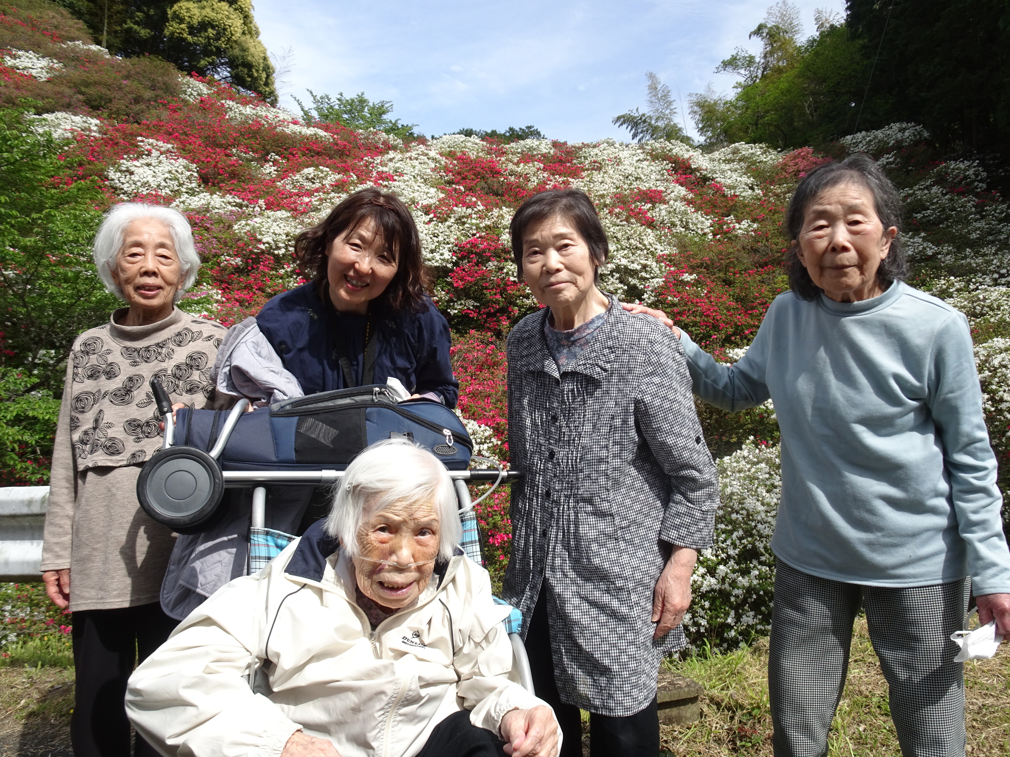 赤や白のツツジをバックに撮った利用者さんたちとワーカーの写真