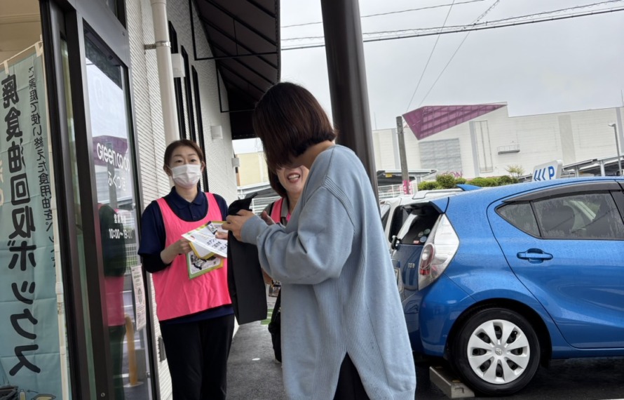 グリーンコープ福津店の入り口でお客様にワーカーがアンケートを渡している