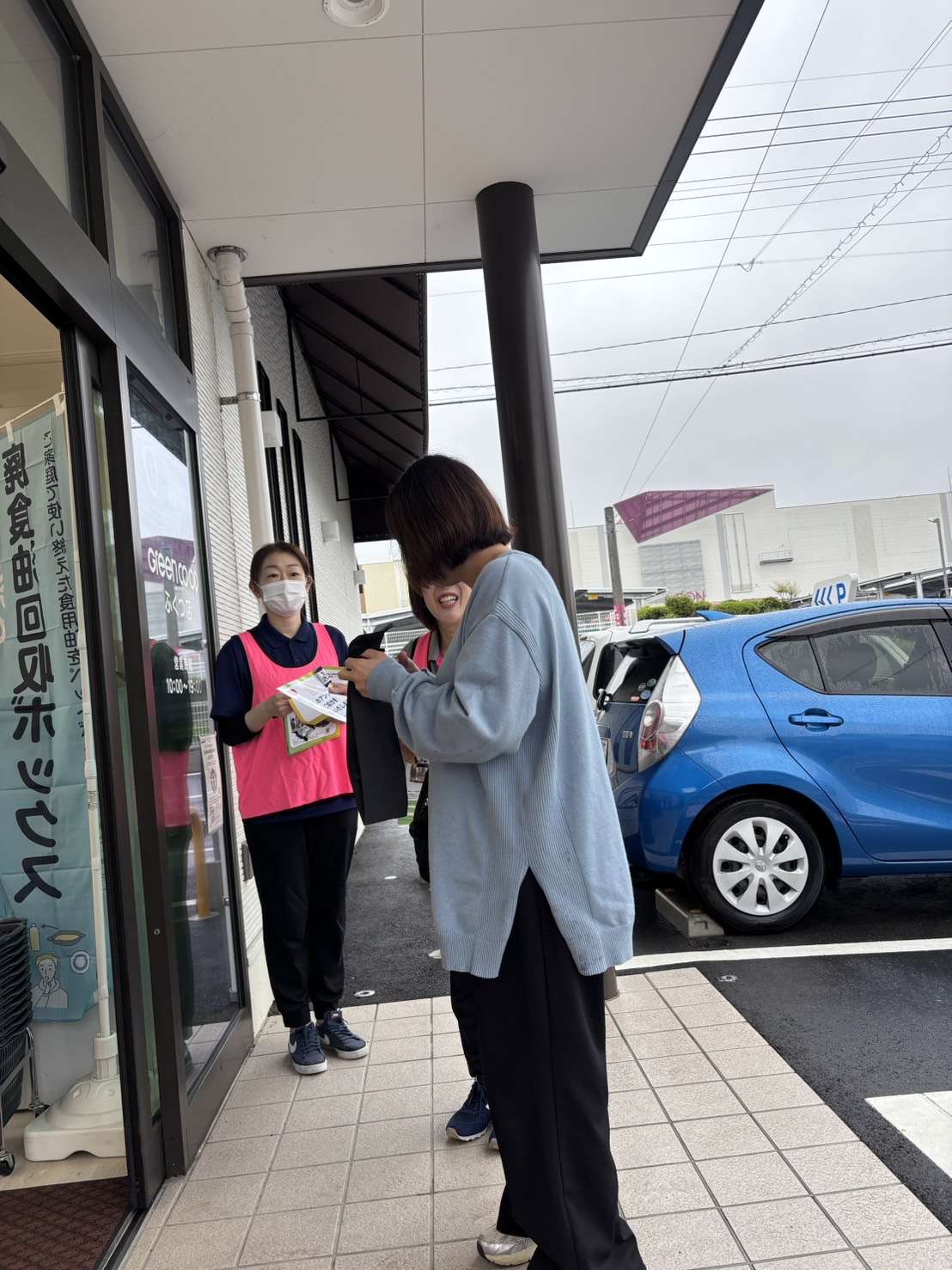 グリーンコープ福津店の入口でお客様にワーカーがアンケートを渡している