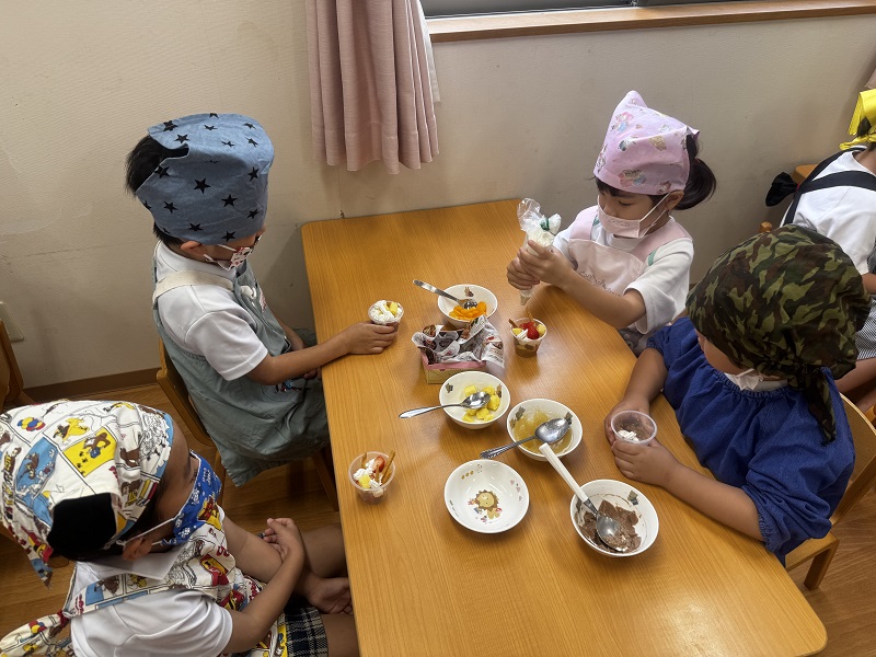 パフェの盛り付けの為にクリームをしぼる子どもとそれを見つめるお友だち