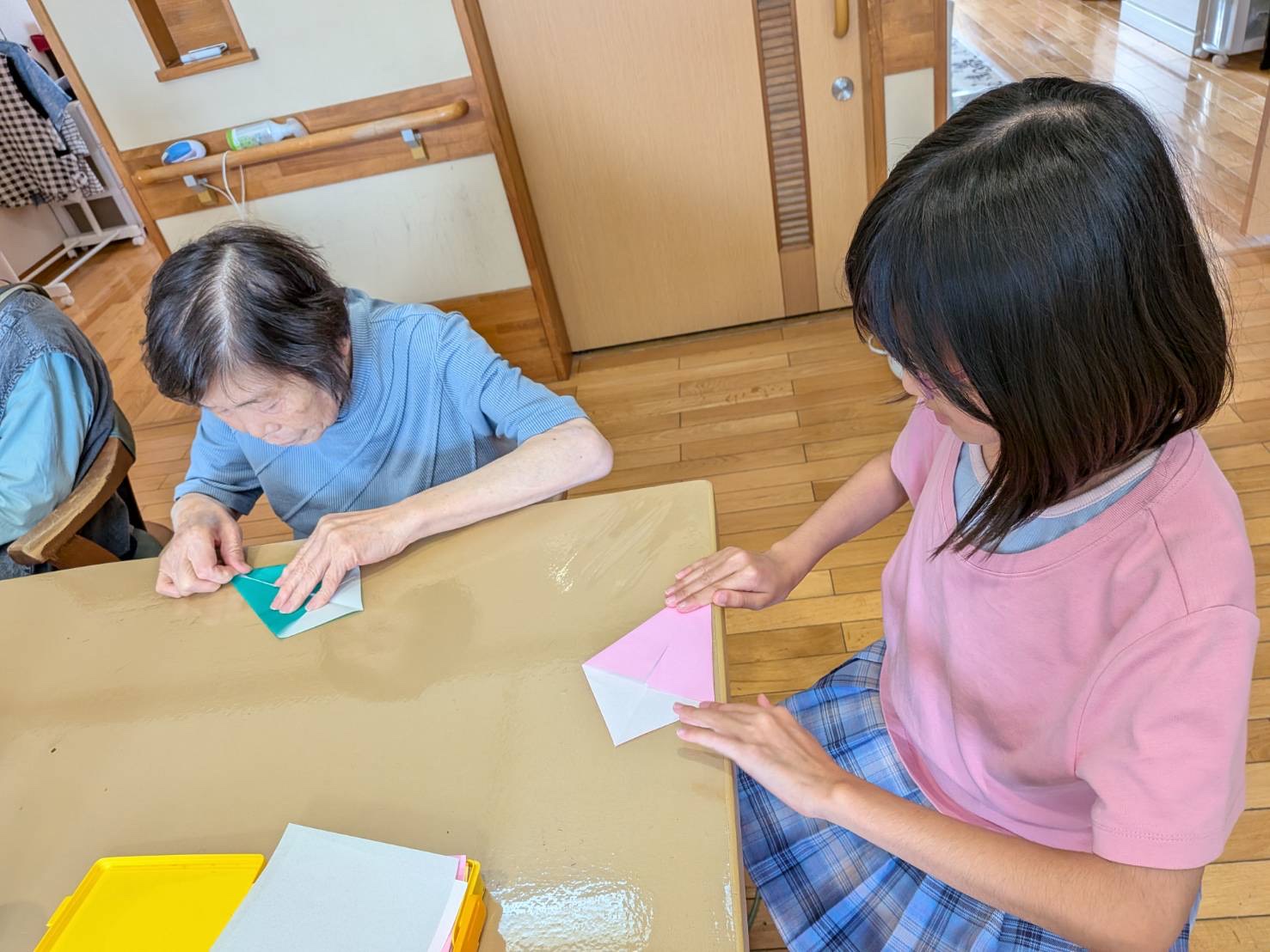 折り紙で紙飛行機を作る利用者さんとワーカーのお子さん