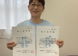 ワーカーがガイドヘルパー養成研修と同行援護従業者養成研修の修了証明書を両手に持ち微笑んでいる