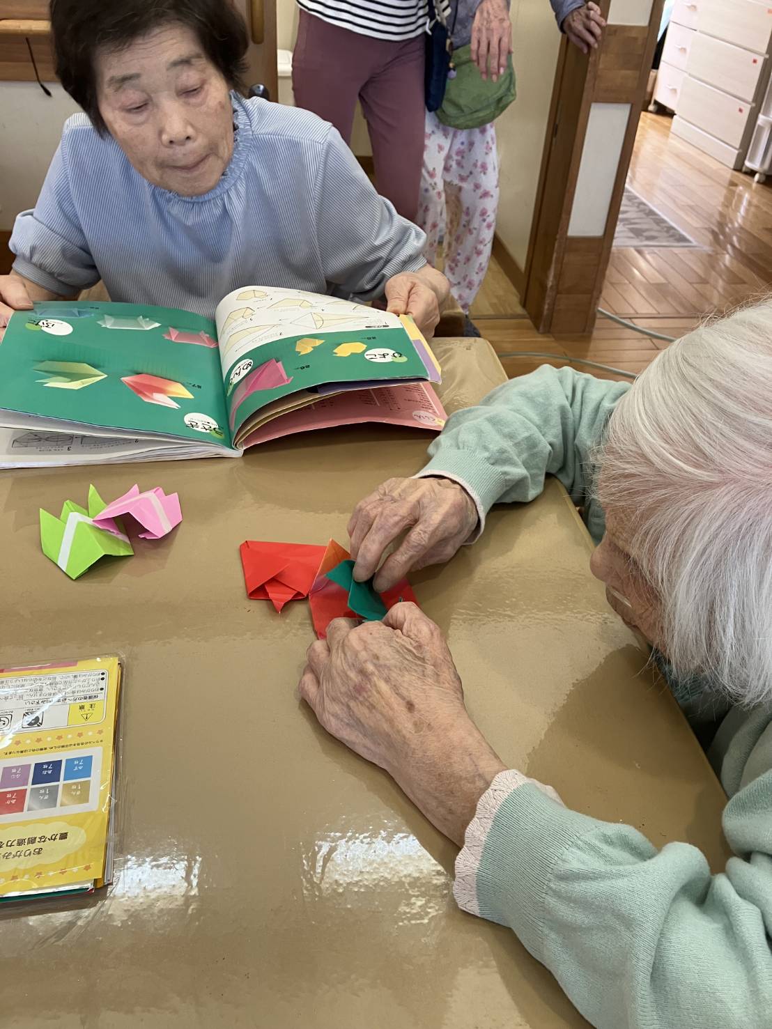 折り紙の本を見ている利用者さんと自分流で折る利用者さん