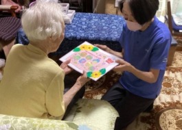 百寿を迎えた利用者様にワーカーがお祝いの色紙を渡している
