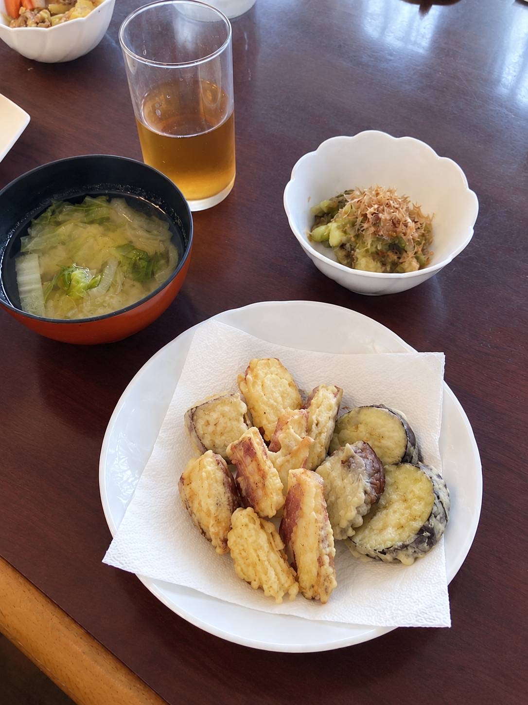 食卓にヘルパーが調理したなすとさつまいもの天ぷらと小鉢には焼きなす、お味噌汁が並べてある。