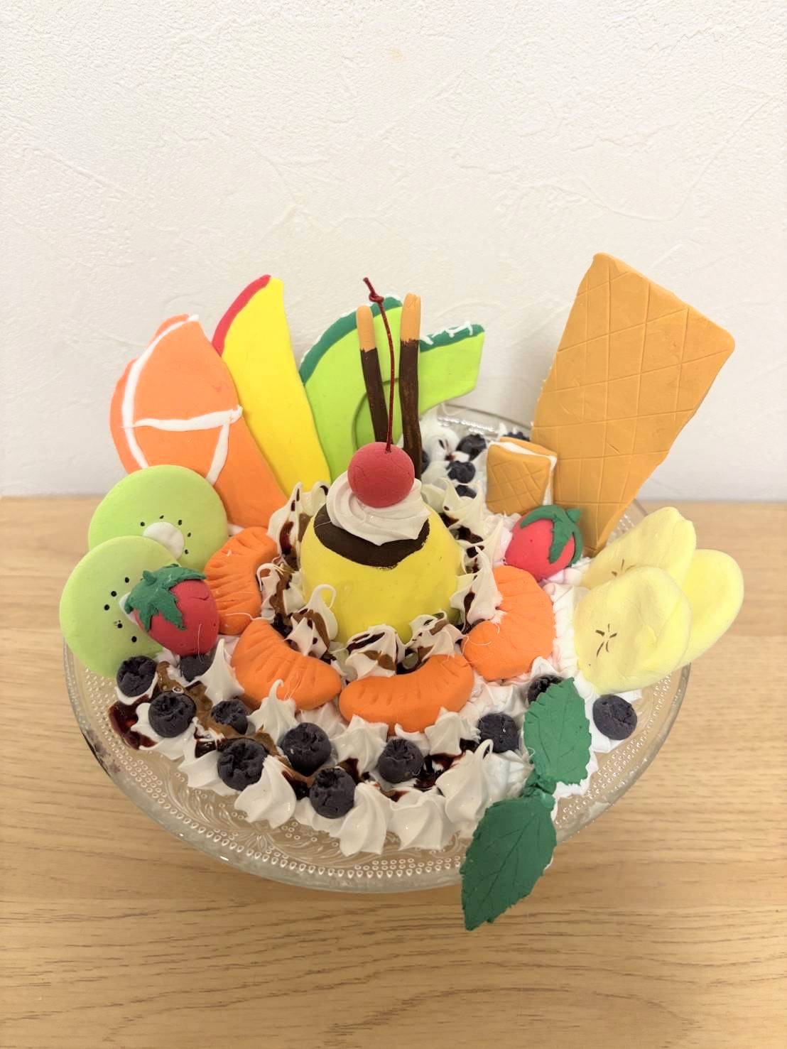 小学4年生の利用者様が粘土で作られたパフェ。真ん中にプリン周りにフルーツやホイップクリーム、ポッキーなどが飾られている