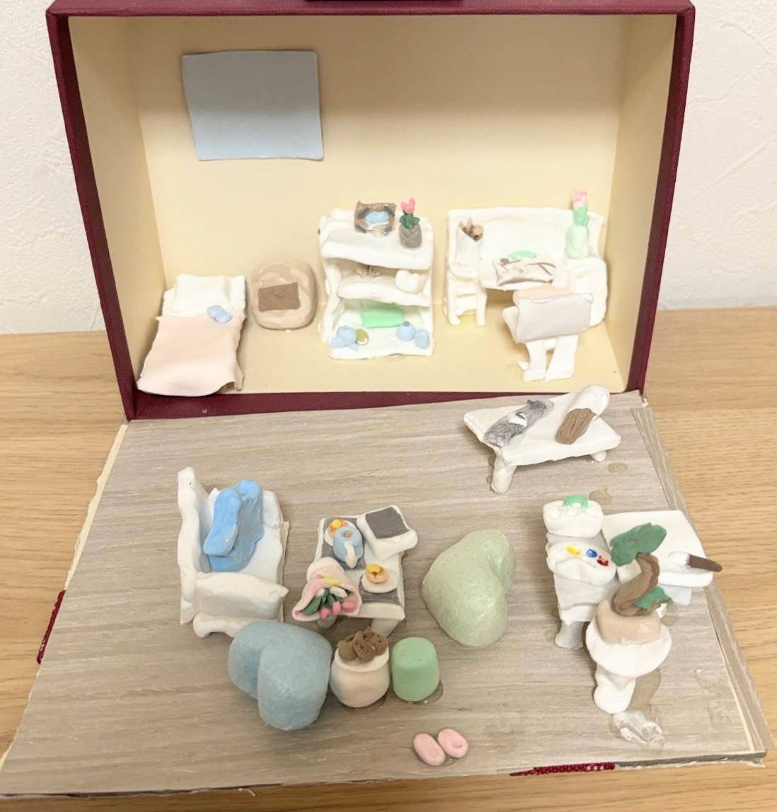 小学4年生の利用者様が粘土で作られたドールハウス。机や椅子、ベットやソファー、テーブルがある。テーブルの上には花束やコップ、食べ物が置かれている。
