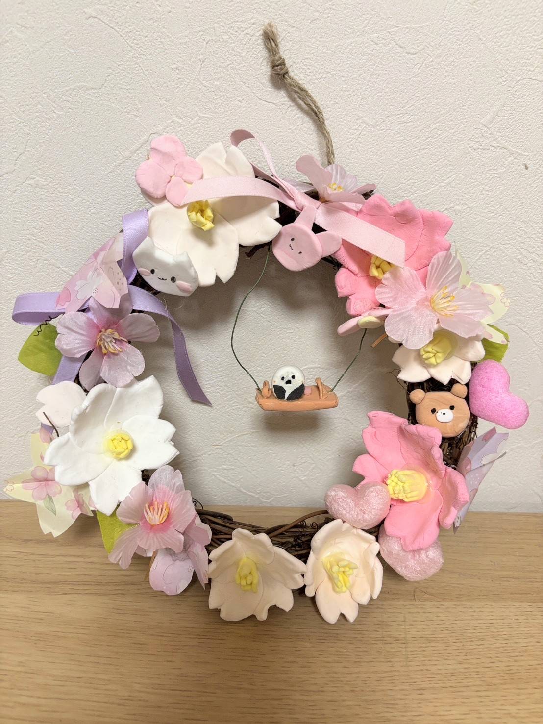 小学4年生の利用者様が粘土で作られたお花のリース。白やピンクの花に熊や猫やうさぎやはーとの飾りがついている。真ん中にブランコに乗った鳥がいる。