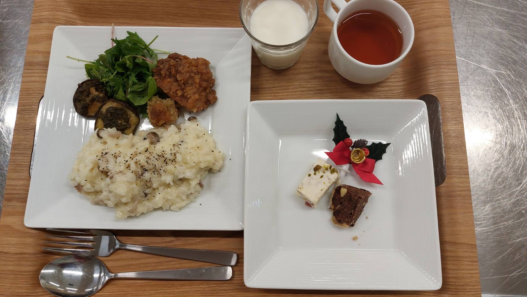 左のお皿にはチキンとクリームリゾット、サラダが盛り付けられています。右のお皿にはクリスマスケーキが2種類盛り付けられています。牛乳とルイボス茶があります。